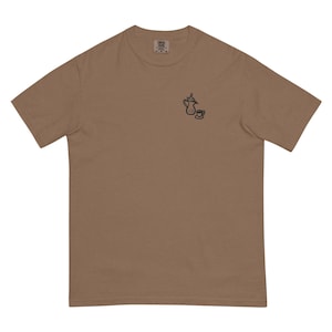 May include: A brown t-shirt featuring a small black illustration of a teapot and teacup. The shirt is made of a soft, comfortable material and has a classic crew neck design. The shirt is a neutral color, suitable for everyday wear.