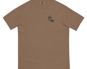 May include: A brown t-shirt featuring a small black illustration of a teapot and teacup. The shirt is made of a soft, comfortable material and has a classic crew neck design. The shirt is a neutral color, suitable for everyday wear.