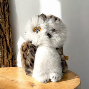 May include: A plush owl toy with brown and white fur. The owl has large, round, yellow eyes and a white belly.