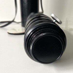 Puede incluir: Un objetivo de c&aacute;mara negro con un anillo plateado alrededor del frente. El objetivo est&aacute; unido a un cuerpo de c&aacute;mara negro.