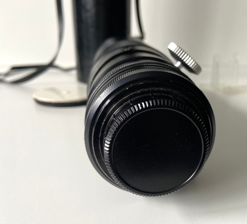 Puede incluir: Un objetivo de c&aacute;mara negro con un anillo plateado alrededor del frente. El objetivo est&aacute; unido a un cuerpo de c&aacute;mara negro.