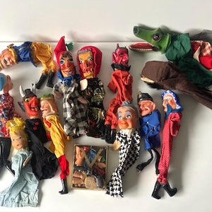 Könnte beinhalten: Eine Sammlung von Vintage-Handpuppen mit bemalten Gesichtern und Stoffkostümen. Die Puppen umfassen Figuren mit Teufelshörnern, einen Drachen, einen Soldaten und eine Frau in einem Kleid. Eine kleine, gerahmte Darstellung von Puppenteilen ist ebenfalls enthalten.