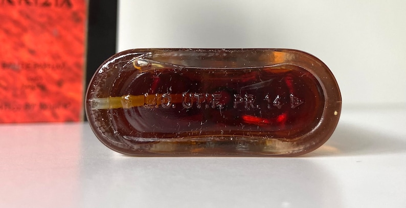 Pu&ograve; includere: Primo piano del fondo di una bottiglia di vetro trasparente con un liquido marrone al suo interno. La bottiglia ha la scritta "M.O. U.S. PAT. PR. 141 D" stampata sul fondo.