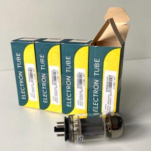 May include: Four rectangular cardboard boxes labeled ELECTRON TUBE in white text on a dark green and yellow background, each featuring a white inventory sticker with barcodes and text. A single glass vacuum electron tube lies in the foreground.