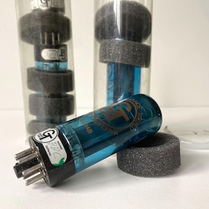 May include: Three Groove Tubes EL34B vacuum tubes with blue glass envelopes and black bases. Each tube features gold printed text including the GT logo and California branding. Two tubes are stored in clear plastic cylinders with foam inserts.