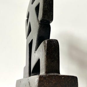May include: A dark, abstract sculpture with a geometric design. The sculpture is made of a dark, possibly stone-like material and features a series of interconnected shapes. It stands on a rectangular base, and the overall form is angular and modern.