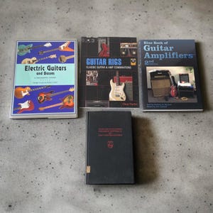 May include: A collection of books about guitars and amplifiers. The books include "Electric Guitars and Basses", "Guitar Rigs", and "Blue Book of Guitar Amplifiers". The books are on a gray surface.