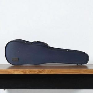 Puede incluir: Un estuche de violín azul marino con asa y detalles metálicos. El estuche está sobre una superficie de madera sobre un fondo blanco. Diseñado para proteger un violín.