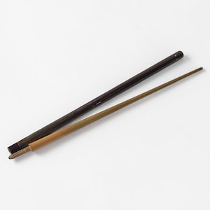 Puede incluir: Dos palillos de pelo de madera. Uno es marrón oscuro, el otro es marrón claro. El palillo marrón oscuro es más grueso y parece ser una funda para el palillo más claro. El palillo más claro es delgado y puntiagudo.