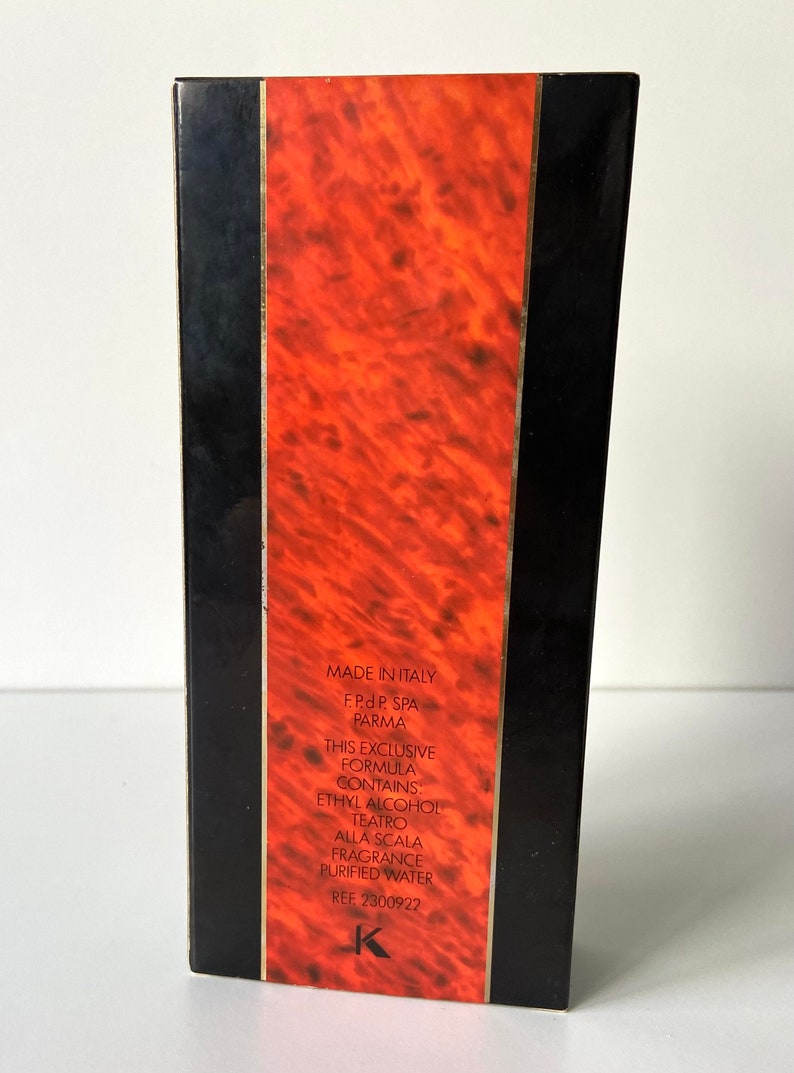 Pu&ograve; includere: Una scatola nera con un design marmoreo rosso e oro. La scatola ha testo bianco che recita "Made in Italy", "F.Pd P. SPA", "PARMA", "This exclusive formula contains: Ethyl Alcohol", "Teatro Alla Scala", "Fragrance", "Purified Water" e "REF: 2300922".