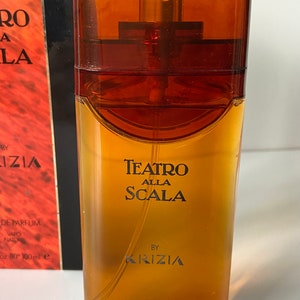 Pu&ograve; includere: Un flacone di profumo Teatro Alla Scala di Krizia in vetro marrone. Il flacone ha un'etichetta dorata con testo nero.