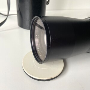 Puede incluir: Un objetivo de c&aacute;mara negro con un anillo plateado y marcas alrededor del borde. El objetivo est&aacute; sobre una superficie circular blanca.