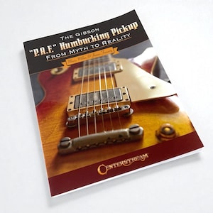 Può includere: Un libro intitolato "P.A.F. Humbucking Pickup From Myth to Reality" con un primo piano di una chitarra Gibson. La copertina ha uno sfondo nero con testo dorato e un bordo bordeaux. La chitarra è marrone e oro.
