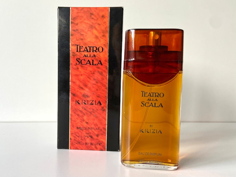 Pu&ograve; includere: Un flacone di profumo Teatro Alla Scala di Krizia in vetro marrone. Il flacone &egrave; rettangolare con un'etichetta dorata e un tappo dorato. La scatola &egrave; rossa e nera con lo stesso testo e logo.