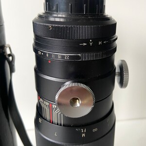 Puede incluir: Un objetivo de c&aacute;mara negro con un anillo de enfoque plateado y un anillo de apertura negro. El anillo de apertura tiene marcas para f/1, f/1.4, f/2, f/2.8, f/4, f/5.6, f/8, f/11, f/16, f/22 y f/45. El objetivo tambi&eacute;n tiene una escala de profundidad de campo y una escala de distancia.