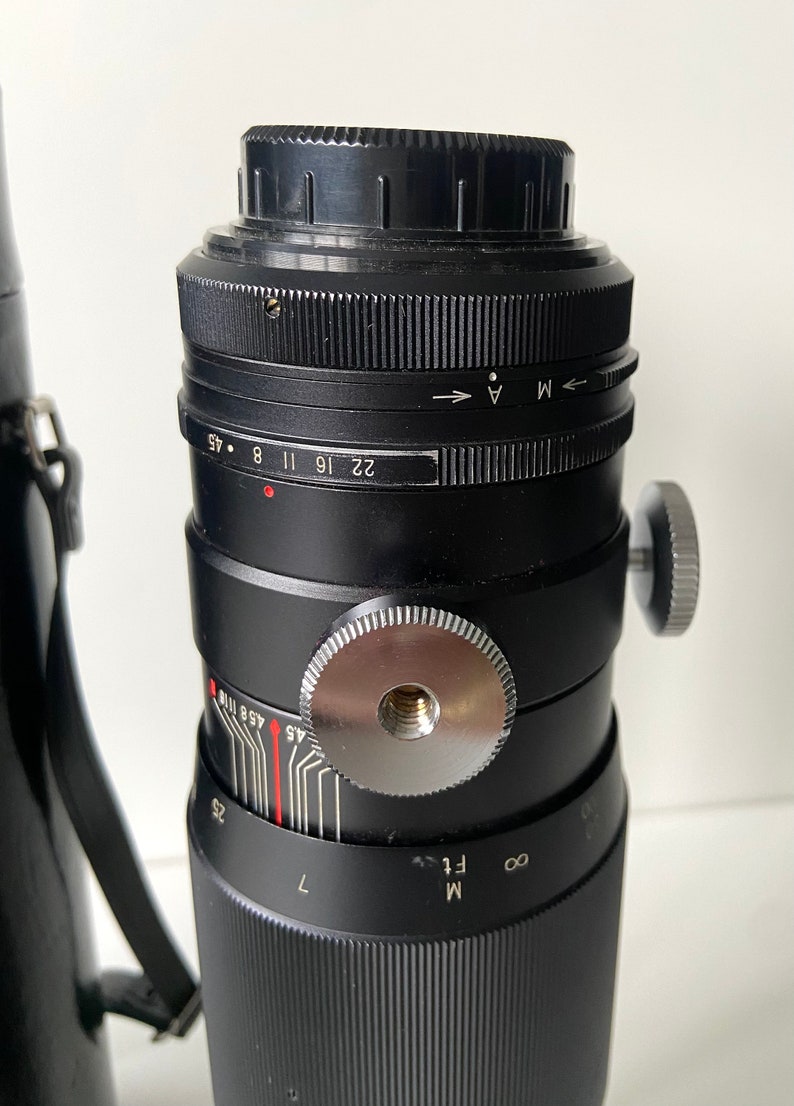 Puede incluir: Un objetivo de c&aacute;mara negro con un anillo de enfoque plateado y un anillo de apertura negro. El anillo de apertura tiene marcas para f/1, f/1.4, f/2, f/2.8, f/4, f/5.6, f/8, f/11, f/16, f/22 y f/45. El objetivo tambi&eacute;n tiene una escala de profundidad de campo y una escala de distancia.