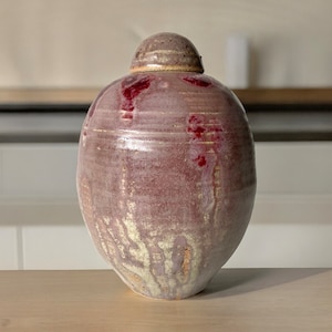 May include: A ceramic jar with a lid, featuring a mottled purple and white glaze with red accents. The jar has a rounded shape and a smooth, glossy finish.