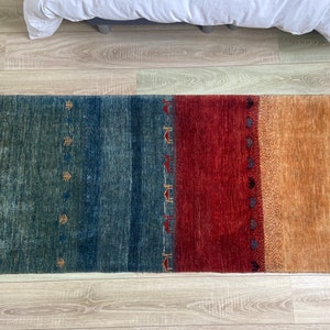 以下が含まれることがあります： 青、赤、茶色のストライプ模様の矩形の敷物。敷物は、小さな繰り返し模様のある幾何学的なデザインです。