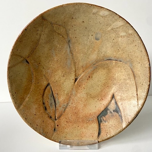 以下が含まれることがあります： 薄い茶色の釉薬と濃い茶色の葉のデザインが施された陶器の皿。皿は丸く、わずかに盛り上がった縁があります。