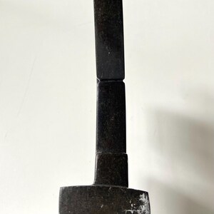 May include: A dark, rectangular sculpture with a curved top. The sculpture is made of a dark, possibly stone-like material. The base is a wider rectangle, and the body is composed of stacked rectangular blocks.