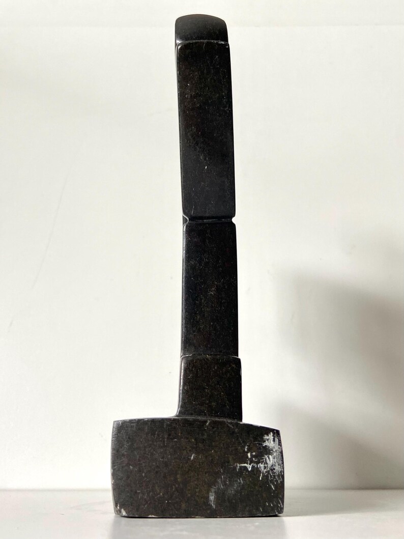 May include: A dark, rectangular sculpture with a curved top. The sculpture is made of a dark, possibly stone-like material. The base is a wider rectangle, and the body is composed of stacked rectangular blocks.