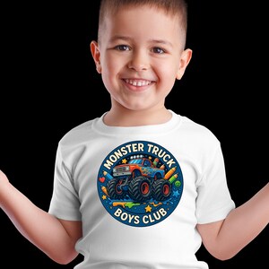 Puede incluir: Camiseta blanca con un dise&ntilde;o de cami&oacute;n monstruo colorido. El dise&ntilde;o circular incluye el texto "MONSTER TRUCK BOYS CLUB", un cami&oacute;n monstruo azul, naranja y rojo, l&aacute;pices y estrellas.