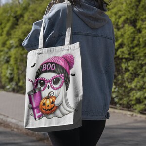 K&ouml;nnte beinhalten: Eine wei&szlig;e Einkaufstasche mit einem rosa und schwarzen Geist, der eine rosa M&uuml;tze mit dem Wort "BOO" tr&auml;gt. Der Geist h&auml;lt einen K&uuml;rbis und ein rosa Getr&auml;nk mit einem Strohhalm.