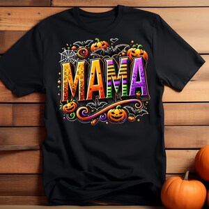 May include: Black t-shirt with a Halloween-themed design featuring the word "MAMA" in colorful, stylized letters surrounded by bats, pumpkins, and spiderwebs.