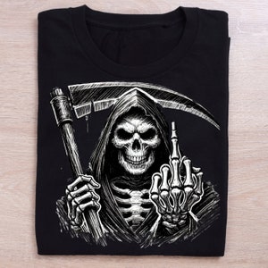 Pode incluir: Camiseta preta com um gr&aacute;fico branco da Morte dando o dedo do meio. A Morte est&aacute; segurando uma foice em uma m&atilde;o.