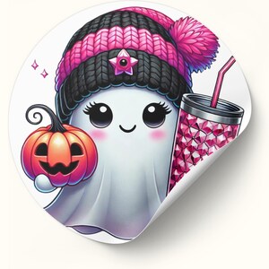 May include: A white ghost wearing a pink and black knit hat with a pom-pom, holding a small orange pumpkin and a pink glittery cup with a straw.