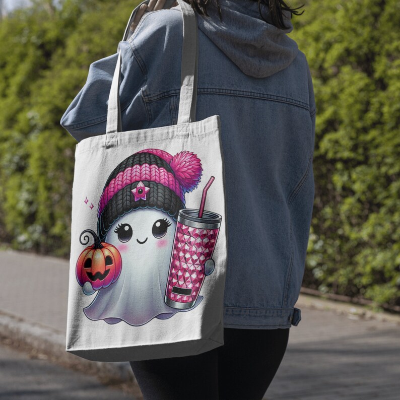 May include: A white tote bag with a pink and black ghost wearing a pink and black hat holding a pink and white cup and a small orange pumpkin. The ghost has a pink nose and big eyes. The bag has a black and white music note design.