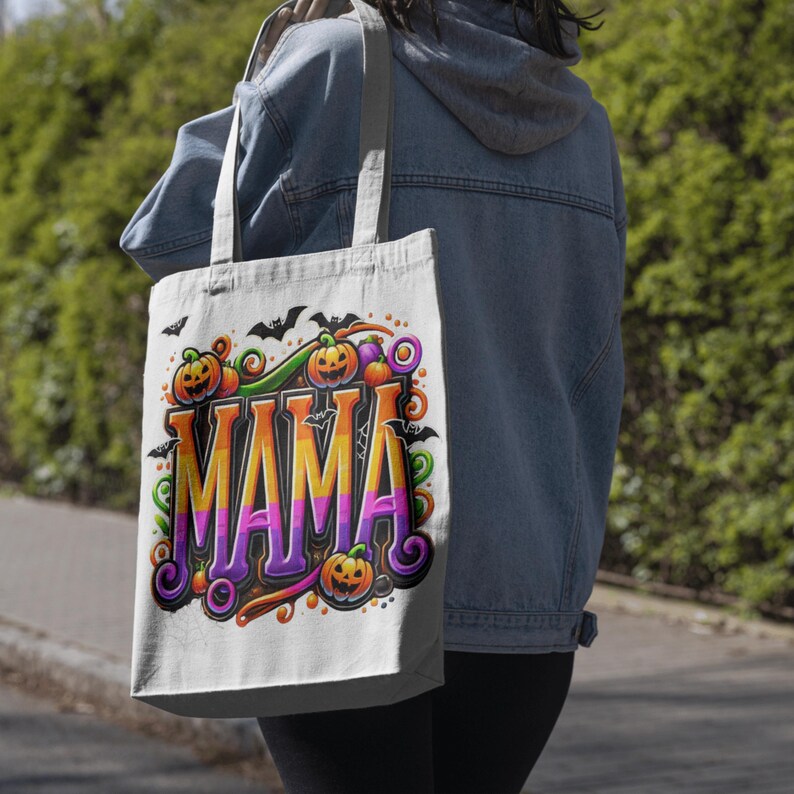Puede incluir: Un bolso tote blanco con un dise&ntilde;o de Halloween. La palabra "MAMA" est&aacute; escrita en naranja, amarillo y morado, rodeada de calabazas, murci&eacute;lagos y espirales decorativas. El bolso tiene una correa de color neutro.