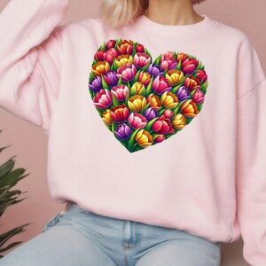 Pode incluir: Um moletom rosa claro com um design em forma de cora&ccedil;&atilde;o feito de tulipas coloridas. As tulipas s&atilde;o em tons de vermelho, laranja, amarelo, roxo e rosa. O moletom &eacute; de cor rosa claro s&oacute;lido.
