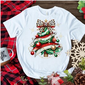 May include: White t-shirt with a Christmas tree design. The tree is decorated with red and green ornaments, a leopard print bow, and gold ribbon.