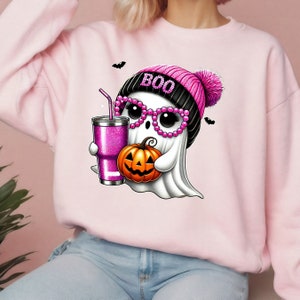 K&ouml;nnte beinhalten: Rosafarbener Pullover mit einem niedlichen Geist, der eine rosa-schwarze M&uuml;tze mit dem Wort "BOO" tr&auml;gt. Der Geist h&auml;lt einen K&uuml;rbis und einen rosa Glitzerbecher mit einem Strohhalm.