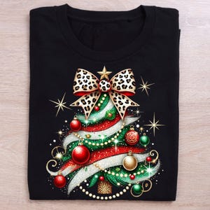 May include: Black t-shirt with a Christmas tree design. The tree is decorated with a leopard print bow, red and green ornaments, and white and gold glitter.