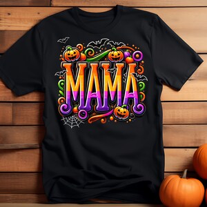 Puede incluir: Camiseta negra con un dise&ntilde;o de Halloween. La palabra "MAMA" se muestra en letras grandes y degradadas, rodeada de calabazas, murci&eacute;lagos y una telara&ntilde;a. El dise&ntilde;o presenta acentos naranjas, morados, verdes y blancos, creando un aspecto festivo.