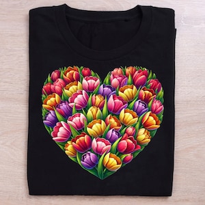 Pode incluir: Camiseta preta com um design em forma de cora&ccedil;&atilde;o feito de tulipas coloridas. As tulipas s&atilde;o em tons de rosa, vermelho, amarelo e roxo, com folhas verdes. A camiseta est&aacute; dobrada cuidadosamente.