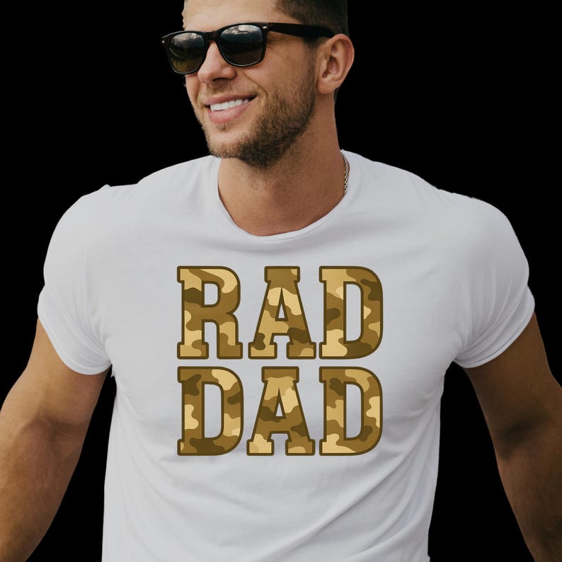 May include: White t-shirt with the words "RAD DAD" in a camouflage pattern. The text is in a bold, blocky font. The shirt is a crew neck style.