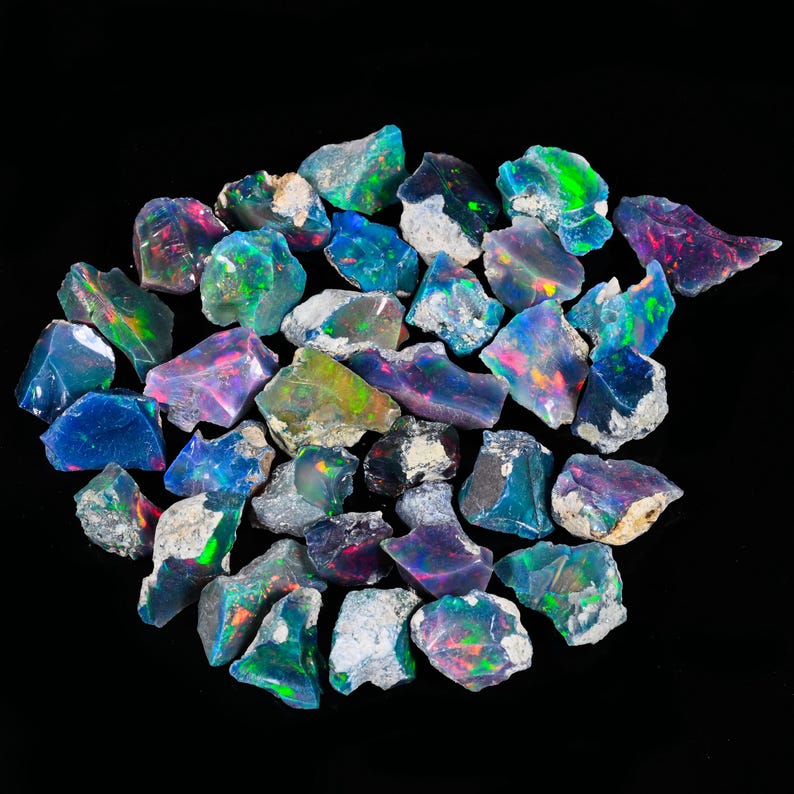 May include: A collection of rough-cut opal gemstones, showcasing a vibrant display of colors including blues, greens, pinks, and purples. The opals are set against a black background, highlighting their iridescent qualities. These natural stones vary in size and shape.