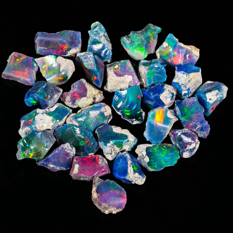 May include: A collection of raw opal gemstones, displaying a variety of colors including blue, green, red, and purple. The opals have a rough, natural texture and are set against a black background.