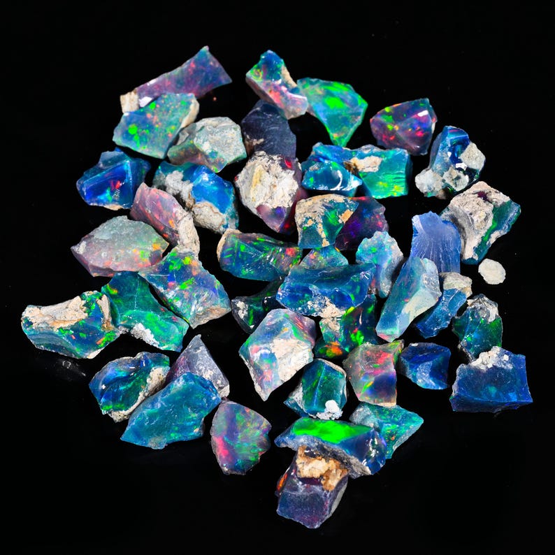 May include: A collection of raw opal gemstones, displaying a vibrant array of colors including blues, greens, and flashes of red and purple. The rough stones have a natural, unpolished appearance, with a mix of opaque and translucent sections.