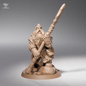 Peut inclure: Figurine miniature de guerrier nain de couleur beige, tenant une grande arme. Le nain a une longue barbe, une armure détaillée et est posé sur une petite base ronde. La figurine est probablement destinée aux jeux de table ou à la collection.
