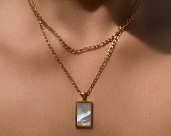 May include: A gold chain necklace with a rectangular pendant featuring a white mother-of-pearl inlay.
