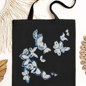 May include: Black tote bag with a white and blue butterfly design. The butterflies are arranged in a cluster on the front of the bag.