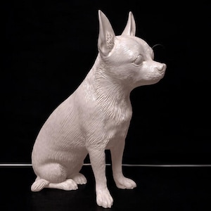 Peut inclure: Une figurine de Chihuahua blanche en position assise, les oreilles dressées et les yeux fermés. La statue de chien est placée sur un fond noir, avec une fine ligne argentée horizontale. La figurine est un objet décoratif.