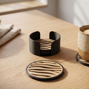 May include: A set of round coasters featuring a light wood top with horizontal wavy cutouts and a black circular frame. The set includes a matching black cylindrical holder for storage, with one coaster placed flat and another supporting a ceramic mug.