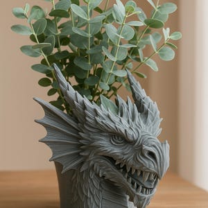 Può includere: Un vaso per piante a forma di testa di drago grigio con una pianta verde frondosa che cresce dalla cima.