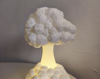 May include: A white mushroom cloud-shaped lamp with a textured, bulbous top and a narrow, ribbed stem base. The lamp emits a soft, warm yellow glow from within, illuminating the structure and highlighting the rounded, cloud-like forms.