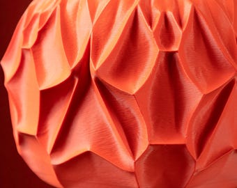May include: Close-up of an orange decorative bowl with a geometric, textured surface. The bowl's design features diamond-shaped facets, creating a play of light and shadow. The color is a vibrant, warm orange.
